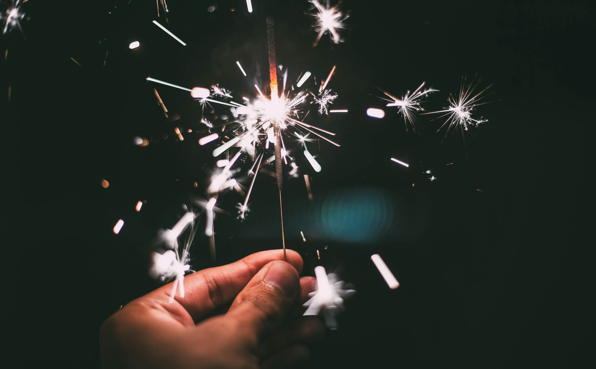 A hand holding a sparkler representing happy new year messages to employees