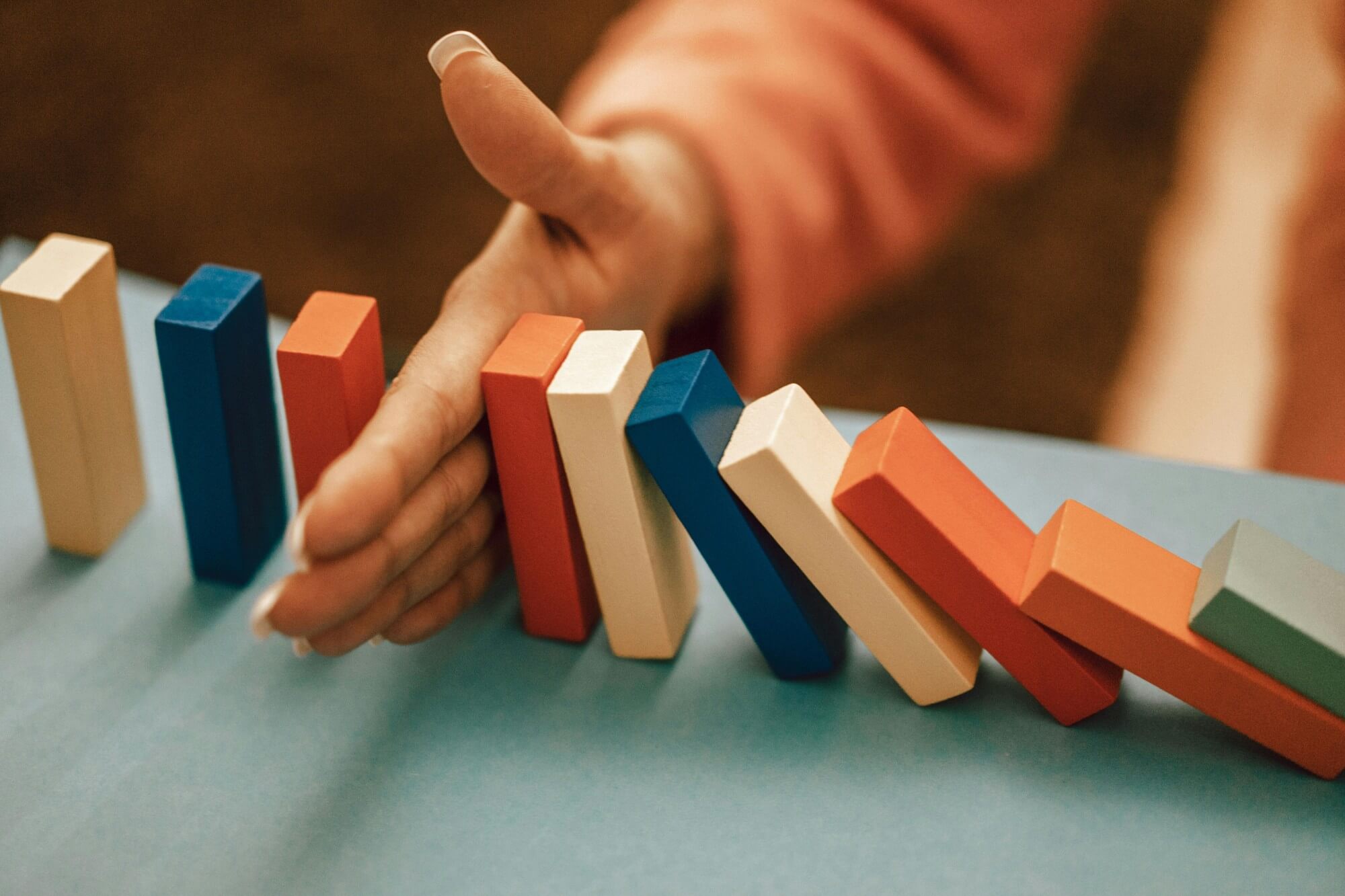 A hand stopping a chain reaction of colorful falling blocks, symbolizing how to avoid common hiring mistakes