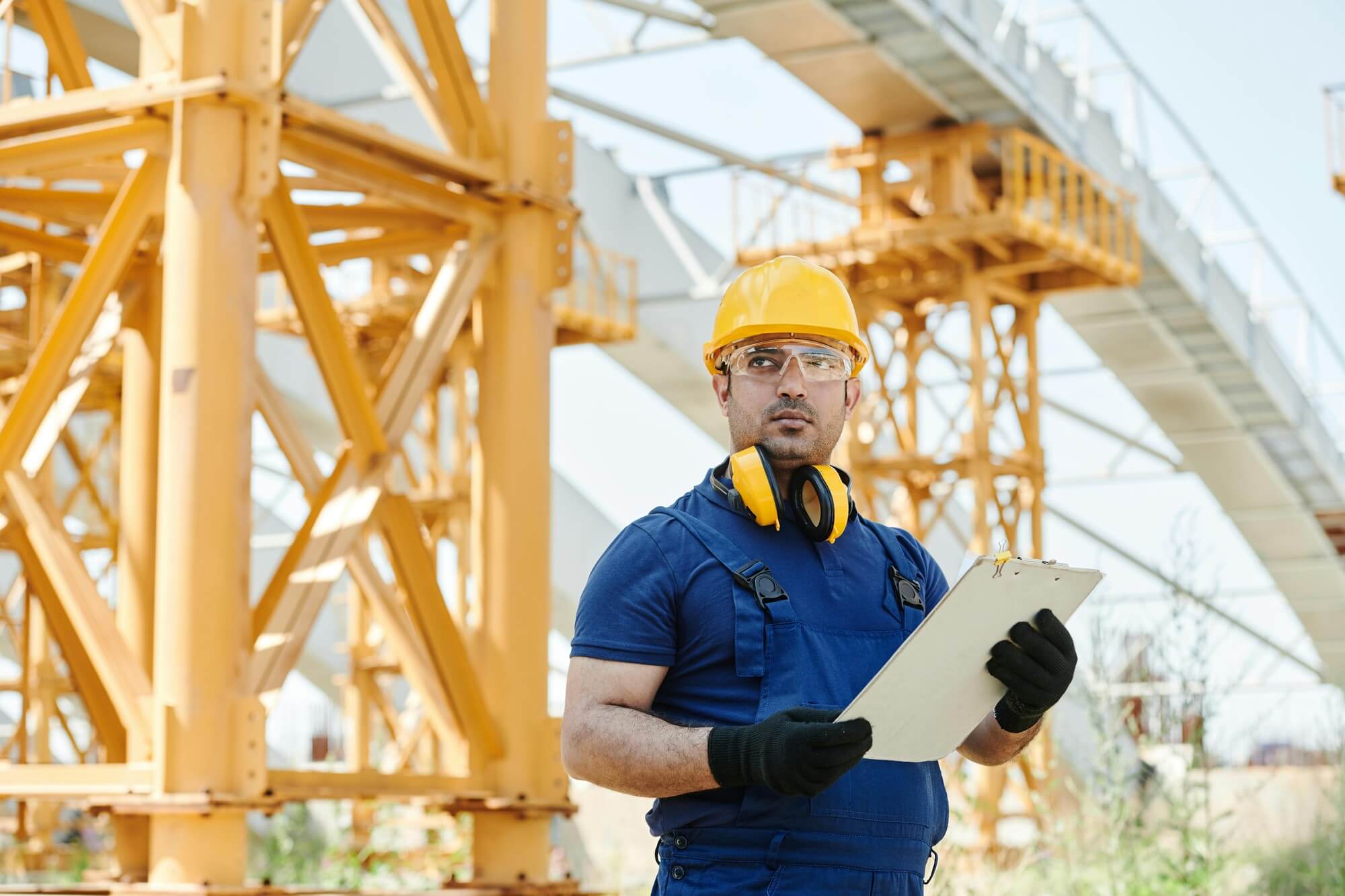 Safety worker with clipboard reviewing contingent workforce compliance documentation at an industrial construction site